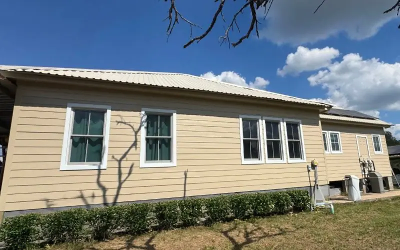 Reemplazo del revestimiento tipo lap de James Hardie en una casa en Bellville, Texas, con revestimiento horizontal de color beige y marcos de ventanas blancos.