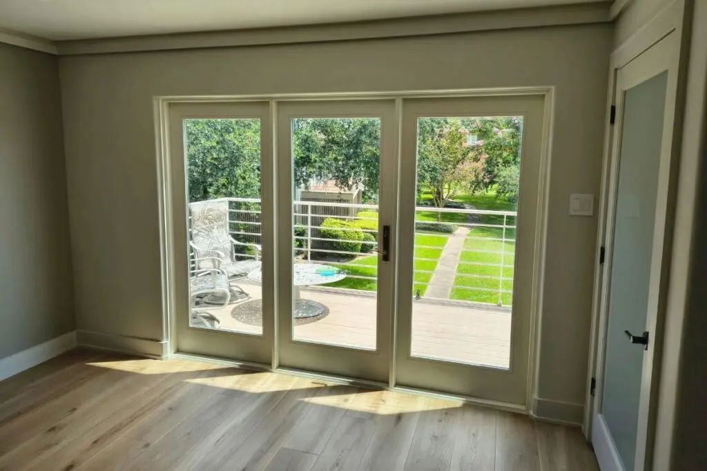 Three-panel hinged patio door with full-length glass panels opening to a backyard.