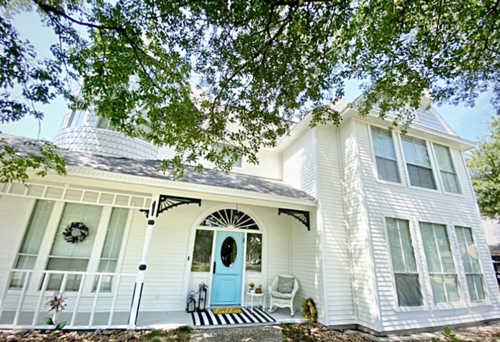 White ornate home with a baby blue front door. Mixed Hardie lap siding and scalloped