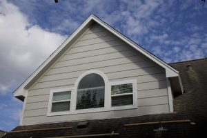 Top portion of a home with white lap siding and three windows