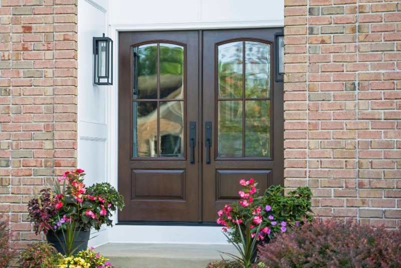 Dark wood double entry doors with glass panels and black hardware on a brick home.
