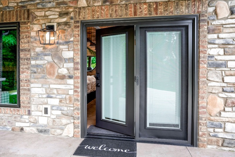 Black ProVia hinged patio door with full-length glass panels installed on a stone and brick home.