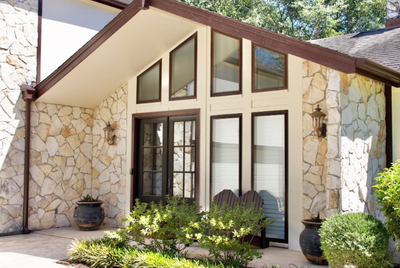 Front of a home with a peak roof and architectural windows in unique shape with brown trim.