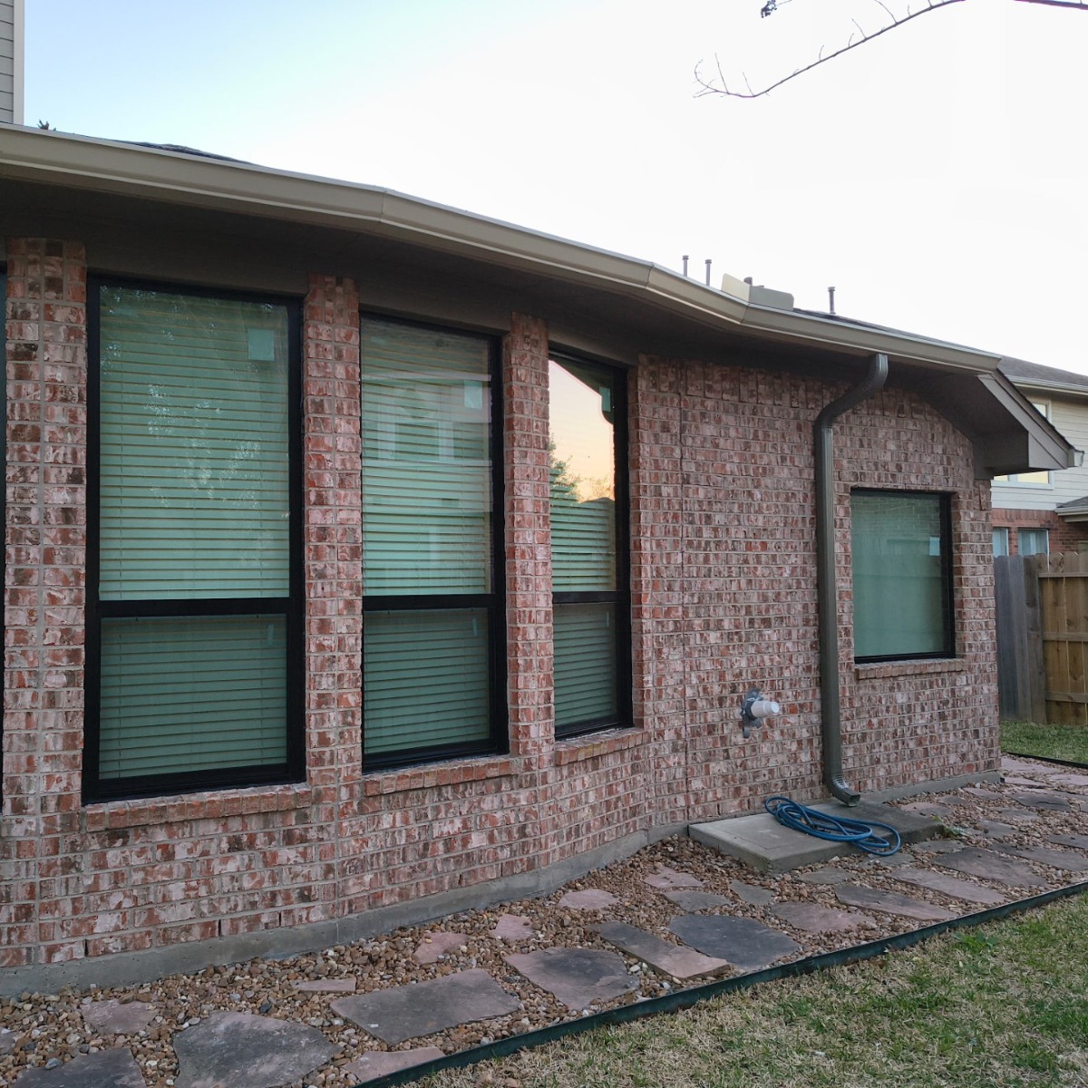 Brick ranch home with black window and gutter and downspouts